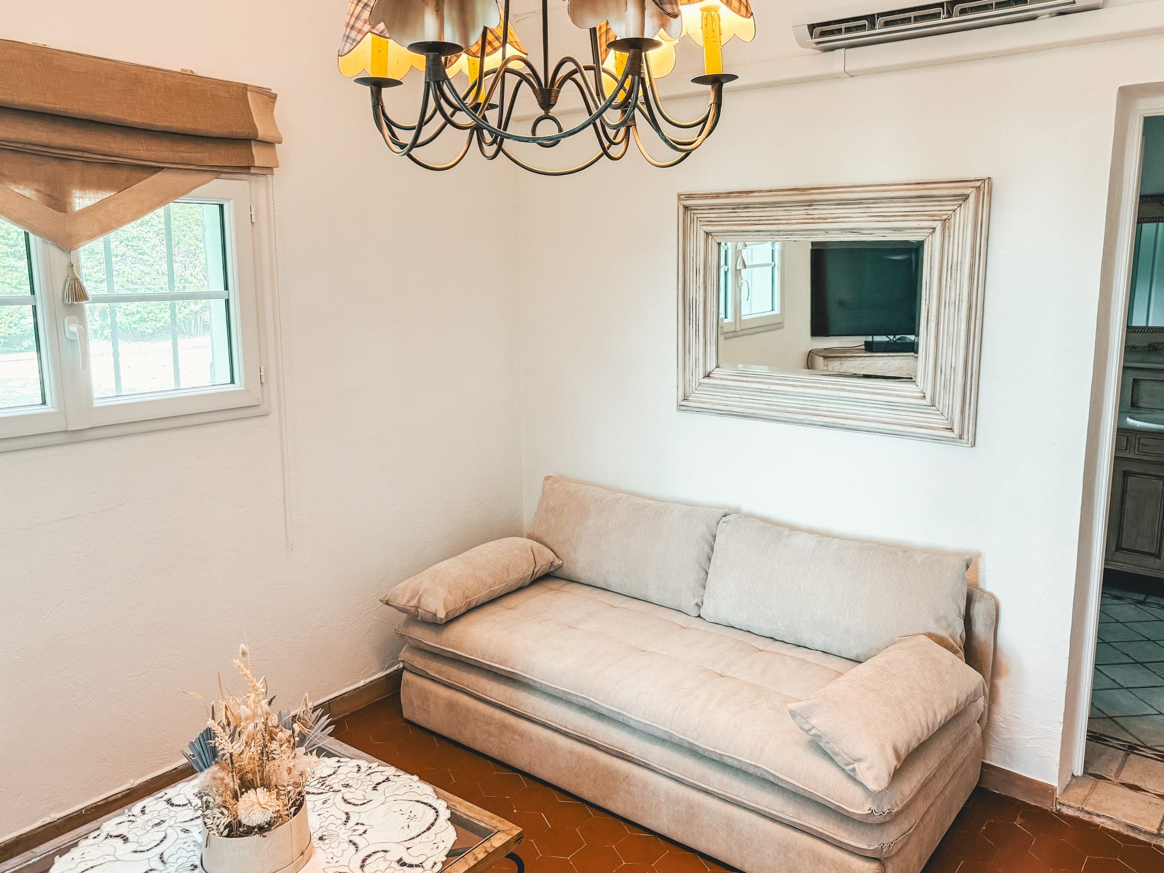 Convertible living room with a linen sofa bed, chandelier, mirror and terracotta floor